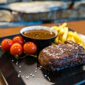 Delicious and juicy steak served with cherry tomatoes, fries, and sauce on a stylish plate.