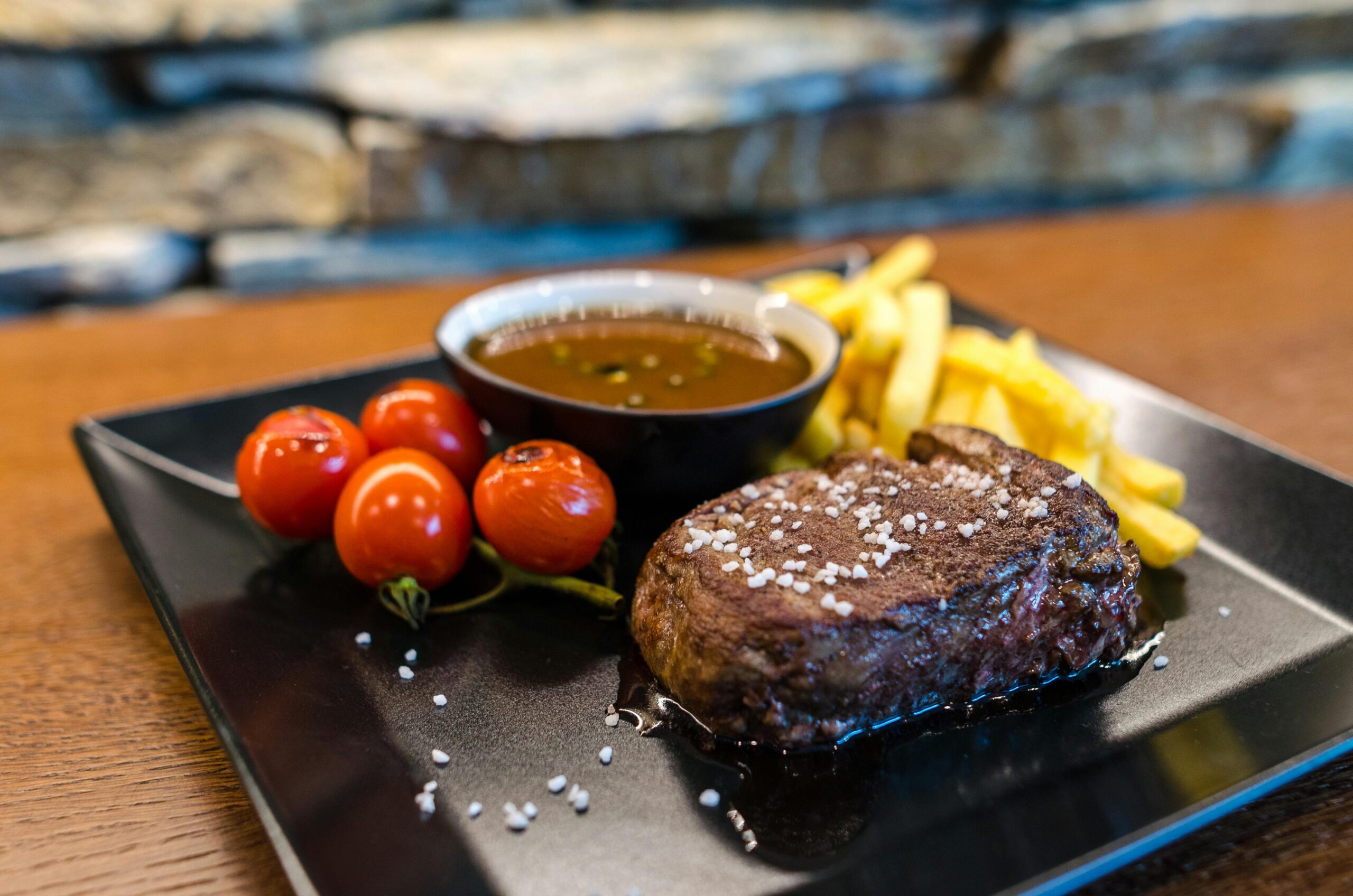 Delicious and juicy steak served with cherry tomatoes, fries, and sauce on a stylish plate.